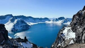 Panoramic view of the deep blue Tianchi crater lake surrounded by snow-capped peaks on Changbai Mountain, China.