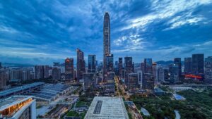 Aerial view of Futian CBD in Shenzhen, China, dominated by the towering Ping An Finance Centre at dusk, with modern skyscrapers and a dramatic cloudy sky.