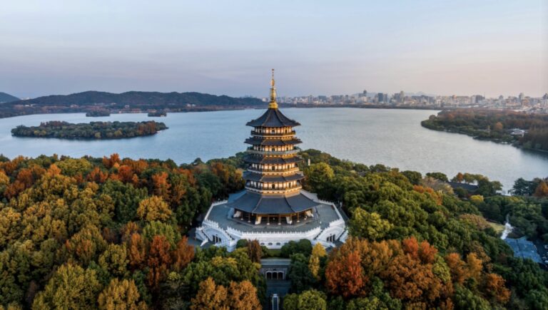 Aerial view of Leifeng Pagoda standing among autumn foliage, overlooking West Lake in Hangzhou, Zhejiang, China.