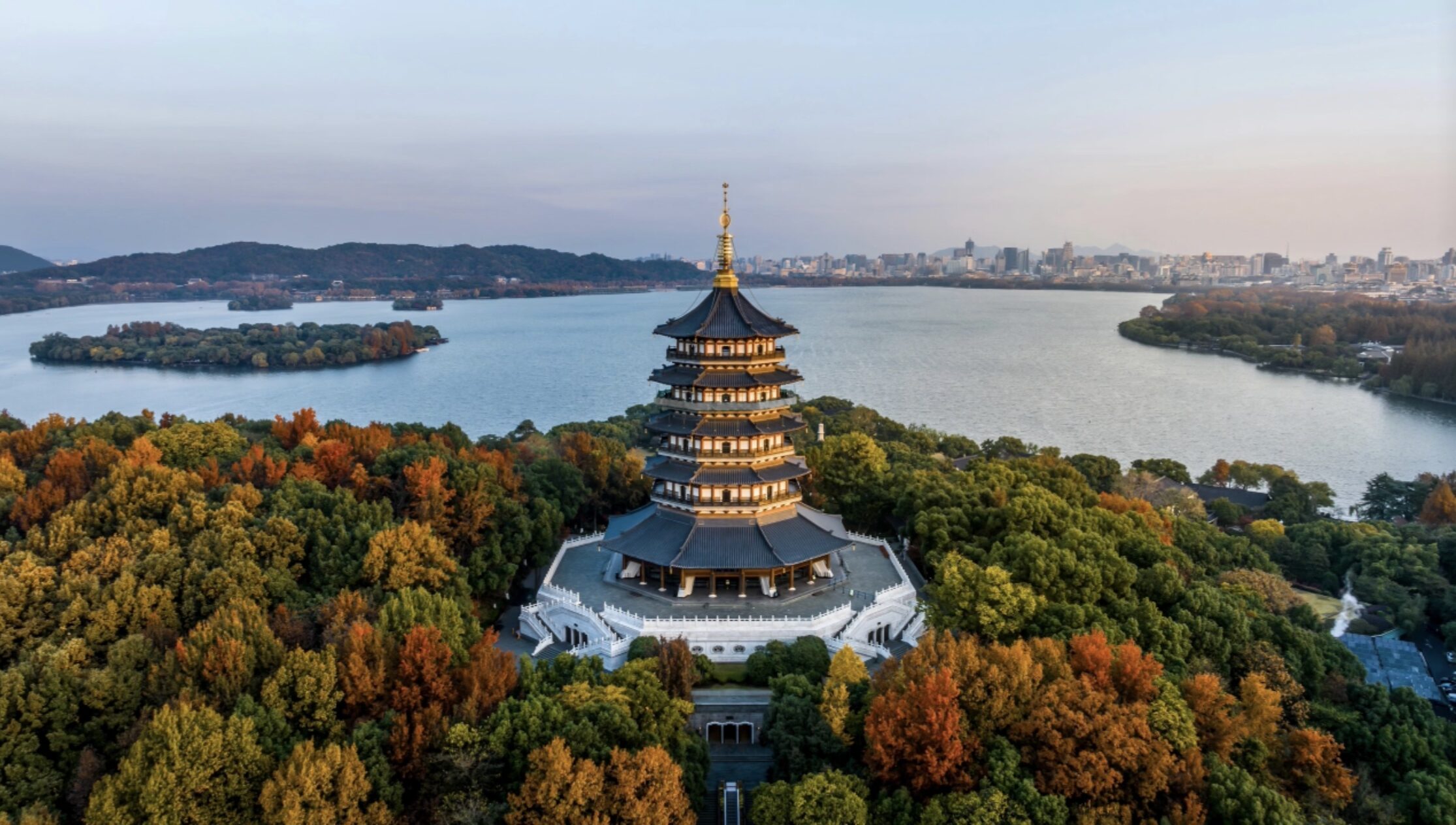 Aerial view of Leifeng Pagoda standing among autumn foliage, overlooking West Lake in Hangzhou, Zhejiang, China.