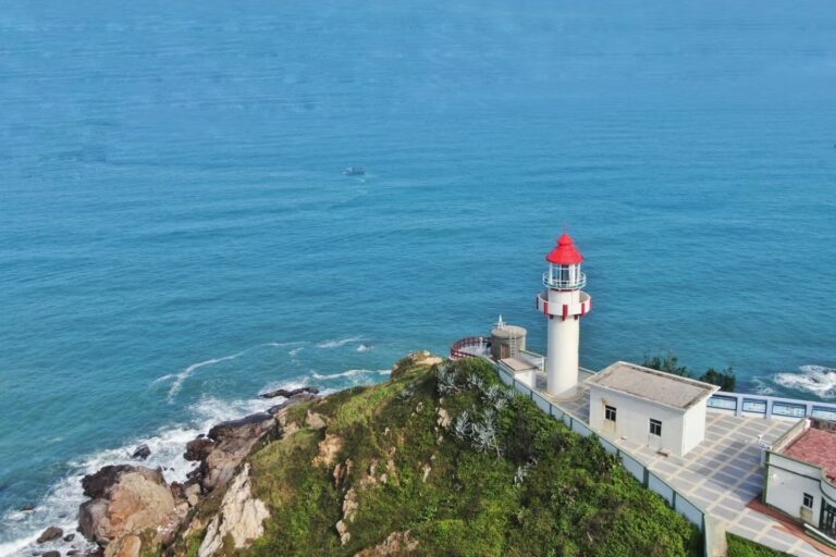 Aerial view of a red-topped lighthouse standing on a rocky headland overlooking the South China Sea in Shantou, Guangdong, China.