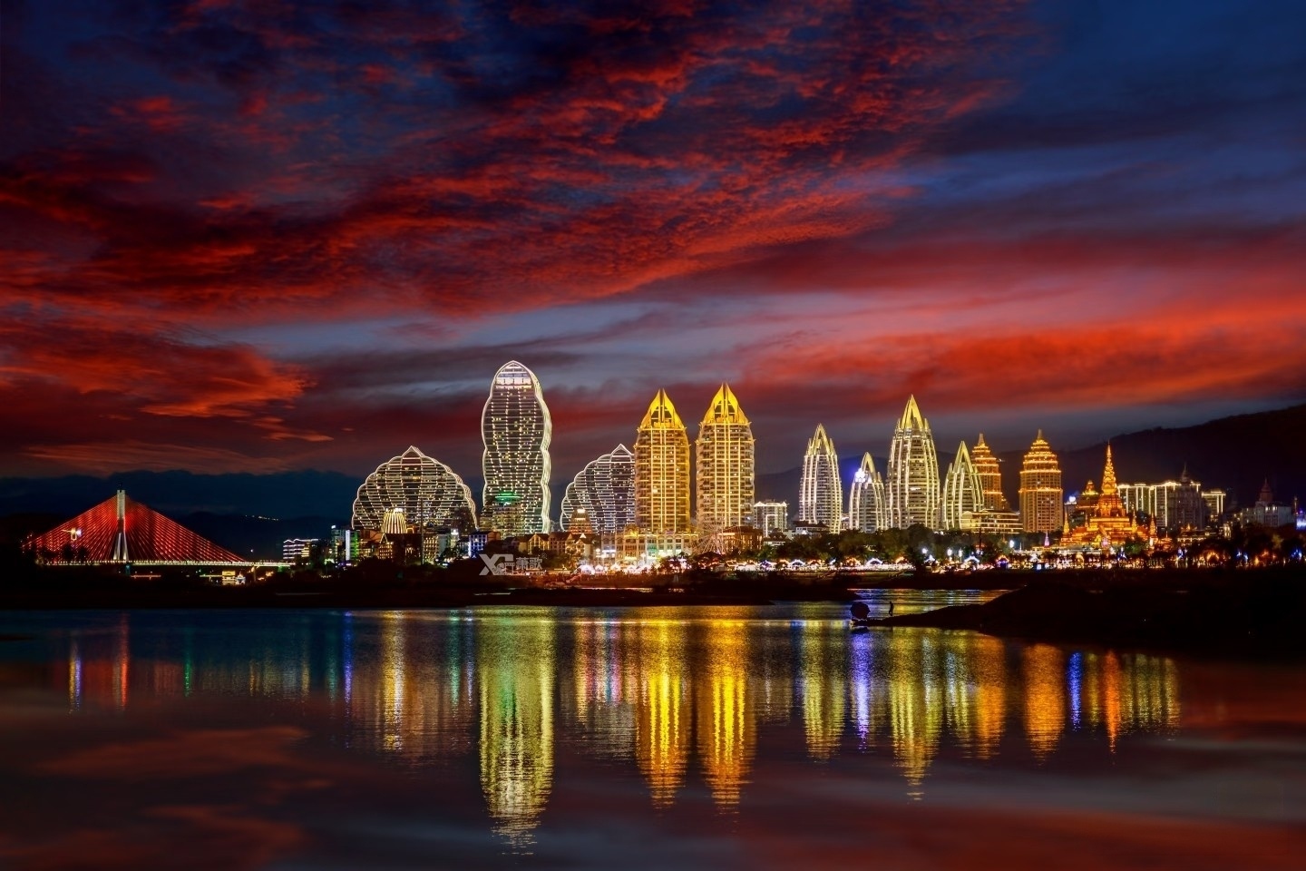 Aerial view of Xishuangbanna's modern skyline with Dai-style architecture, illuminated at dusk along the Lancang River in Yunnan, China.